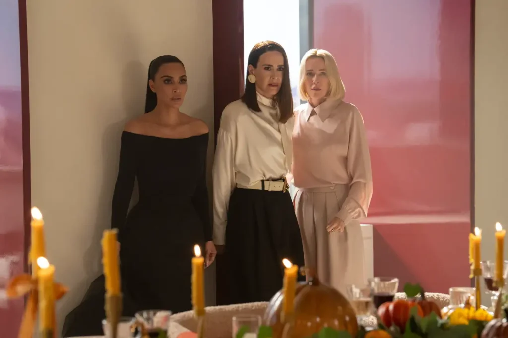 Kim Kardashian, Naomi Watts e Sarah Paulson in abiti eleganti vicino a un tavolo con candele accese e decorazioni autunnali