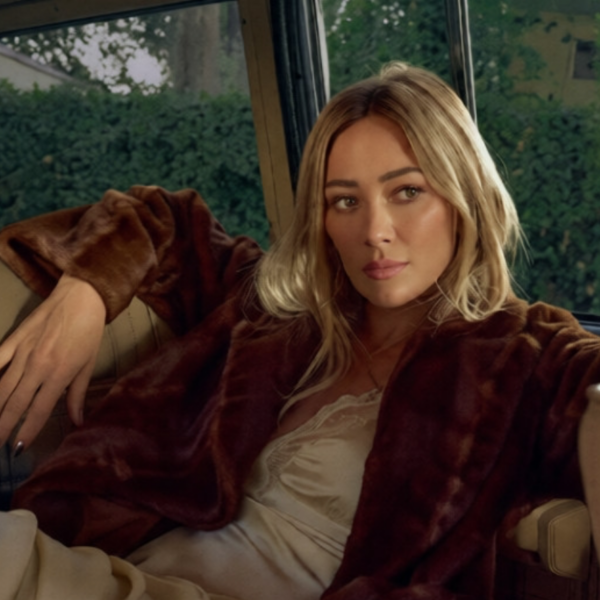 Hilary Duff siede sul sedile posteriore di un'auto indossando una giacca di pelliccia marrone sopra un abito color crema