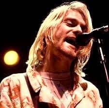 Kurt Cobain canta al microfono durante un concerto dei Nirvana in Italia, con i capelli biondi illuminati da un faretto