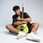 Matteo Trullu, protagonista di JESC 2026, seduto a terra con una chitarra elettrica verde e abbigliamento casual su sfondo