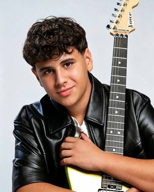 Matteo Trullu, vincitore di The Voice Kids, posa sorridente con una chitarra elettrica indossando una giacca di pelle nera