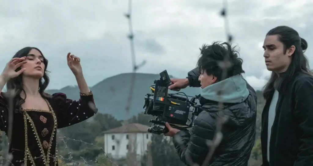 Adele Dell'Erario sul set con una cinepresa ARRI nera riprende un'attrice in costume scuro mentre un giovane osserva su