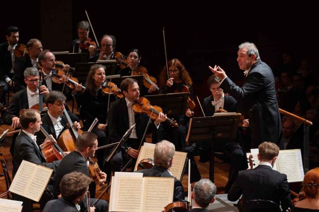 Daniele Gatti sul podio direzione della Staatskapelle Dresden, orchestra d'archi in abiti scuri che suonano spartiti su