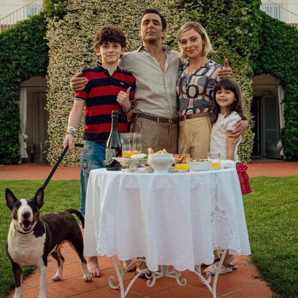 Una famiglia in giardino abbracciata davanti a un tavolo bianco apparecchiato, con due bambini, una donna (Jasmine Trinca) e