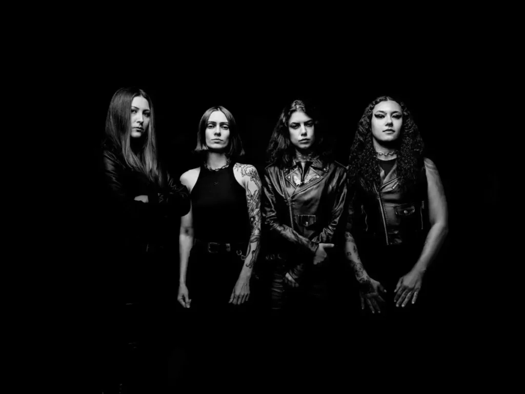 Le quattro musiciste della band Crypta in bianco e nero, in piedi contro sfondo scuro con abiti neri e sguardi severi