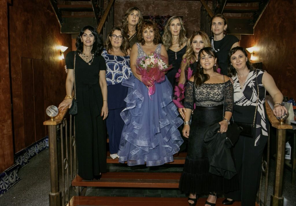 Maria Pia Cappello festeggia il suo compleanno circondata da amiche su una scala, indossando un elegante abito lungo color