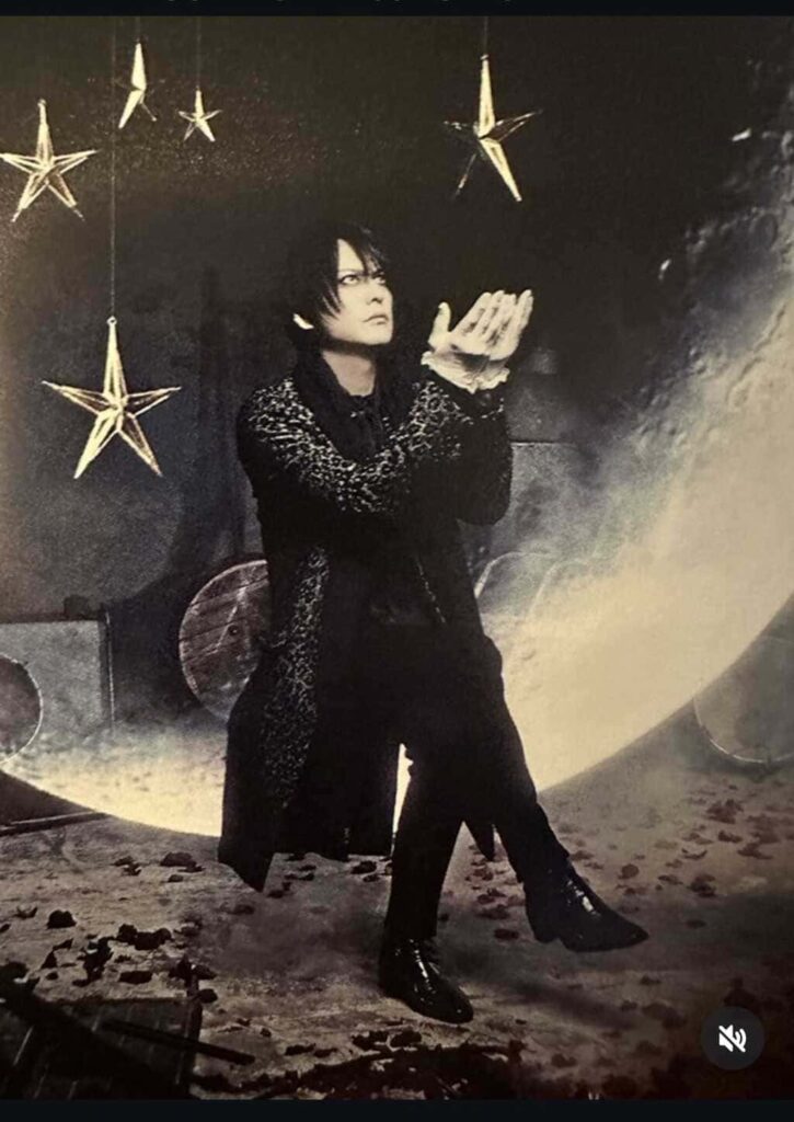 Atsushi Sakurai seduto su una luna crescente stilizzata, circondato da stelle sospese in un'atmosfera dark ed elegante