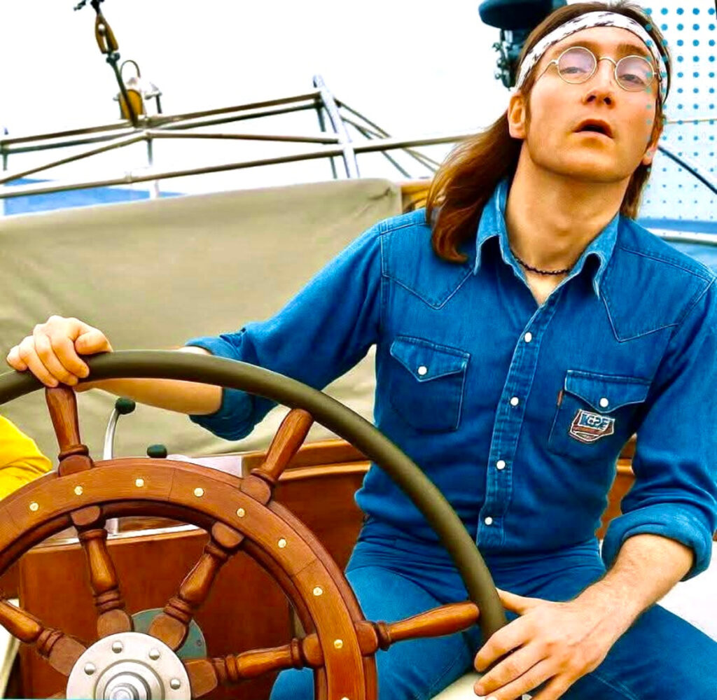 John Lennon con bandana e camicia di jeans al timone di uno yacht da 43 piedi, sguardo verso il mare mentre afferra la ruota