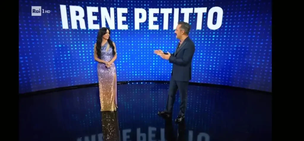 Irene Petitto in un abito lungo scintillante sul palco di Tali e Quali su Rai 1 mentre parla con il conduttore