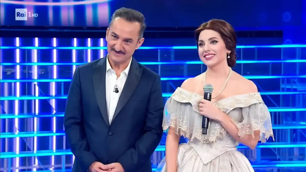 Irene Petitto in abito d'epoca accanto a un uomo in giacca scura sul palco di Tali e Quali su Rai 1