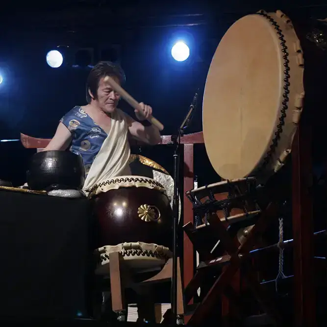 Joji Hirota suona con intensità un grande tamburo taiko durante una performance dal vivo in un'atmosfera suggestiva