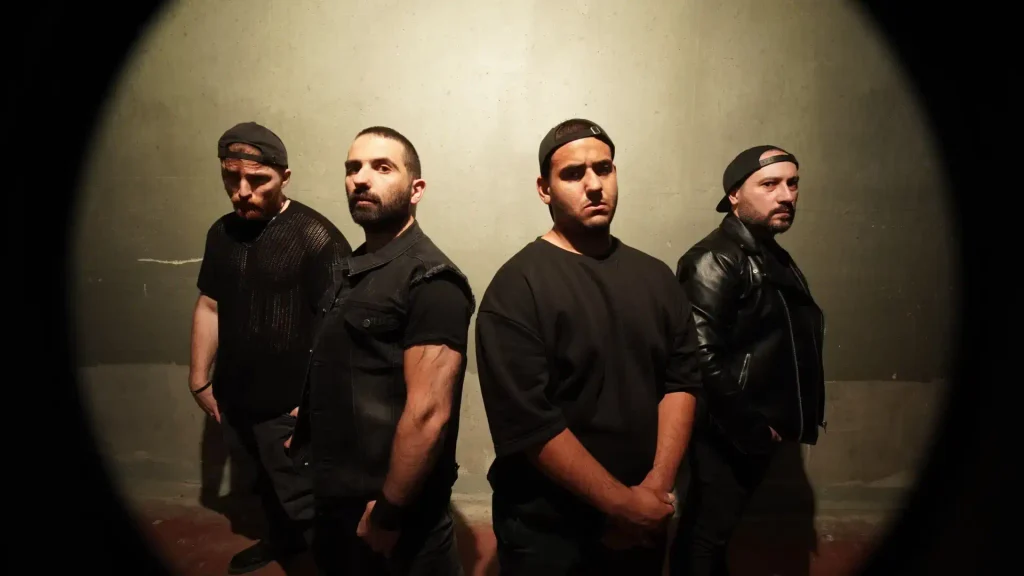 Quattro membri dei Murder One in posa frontale contro una parete grigia, illuminazione circolare e abbigliamento nero