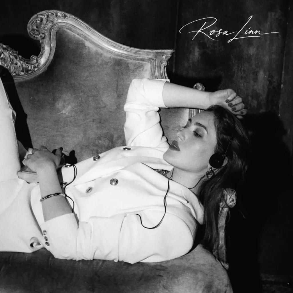 Rosa Linn sdraiata su un divano vintage ascolta musica con le cuffie per promuovere il nuovo singolo Music I Love