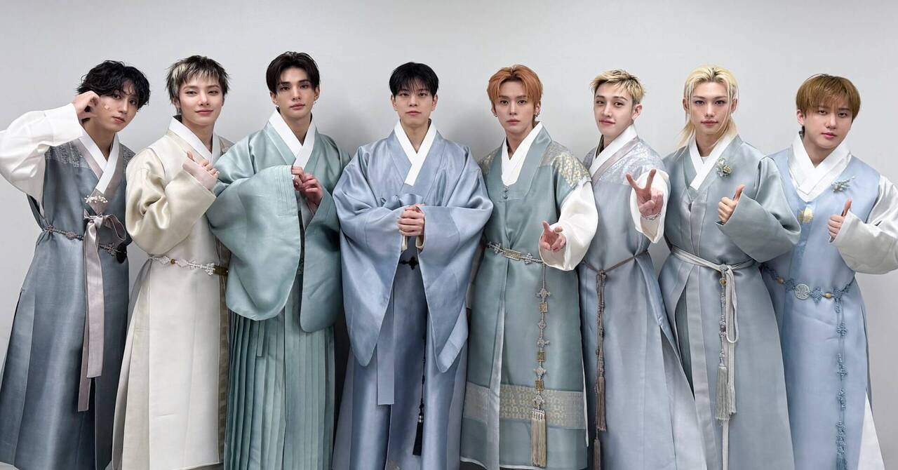 I membri dei Stray Kids in fila, sette giovani con hanbok tradizionali nei toni celeste e grigio, pose con mani a V e