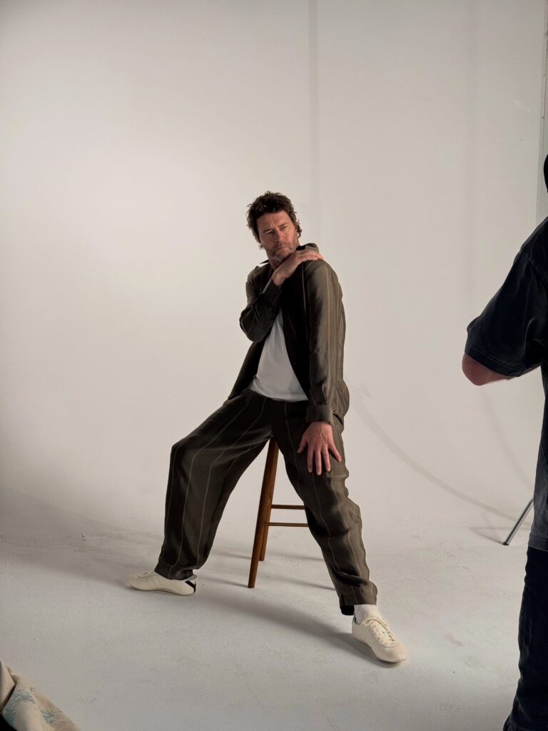 Howard Donald seduto su uno sgabello in studio indossa un completo a righe scure mentre posa per il singolo Higher dei Take