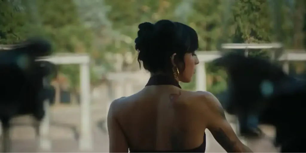 Angelina Mango di spalle, con i capelli raccolti e un abito scuro, in un giardino durante il video di Vita da adulti