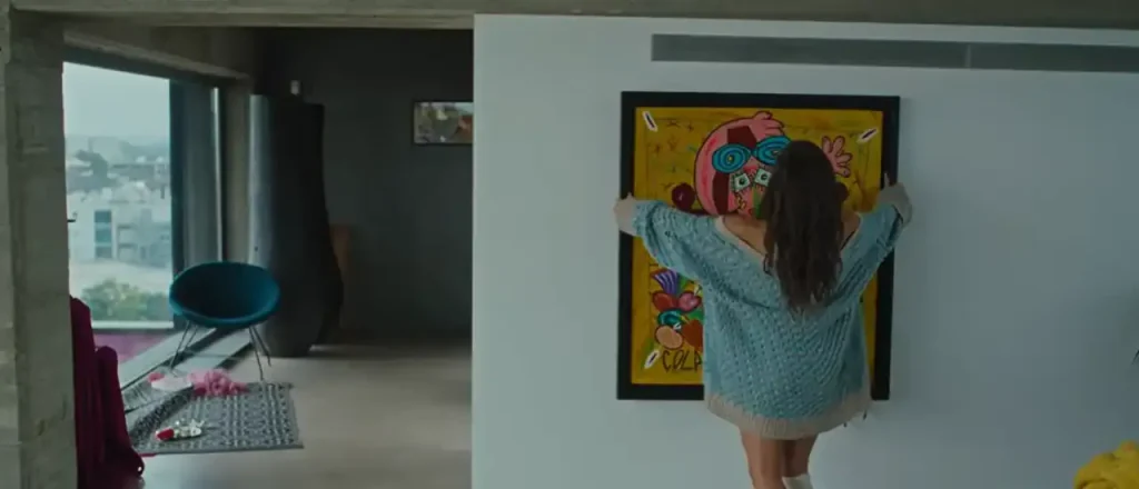 Angelina Mango appende al muro un quadro colorato con uno stile pop art in un interno moderno e luminoso