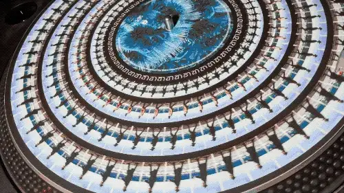 Disco in vinile con grafica a cerchi concentrici bianchi e blu che crea un effetto animato quando gira, testo piccolo