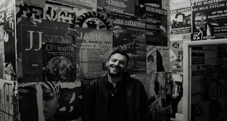 Cesare Cremonini sorride davanti a una parete tappezzata di locandine musicali durante il suo evento cremonini amateur
