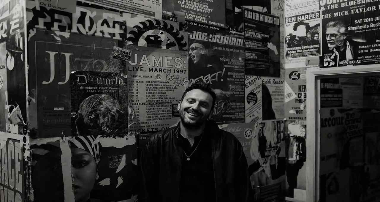 Cesare Cremonini sorride davanti a una parete tappezzata di locandine musicali durante il suo evento cremonini amateur