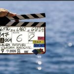 Ciak della serie originale Disney+ Delitto sul Lago di Garda tenuto da una mano davanti alle acque blu del lago