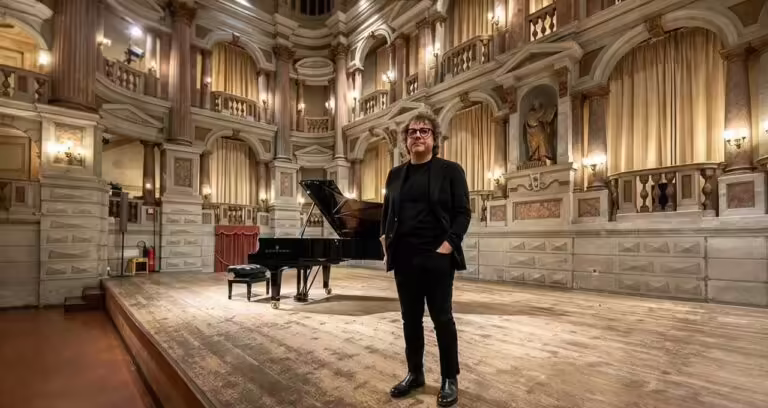 Il compositore Remo Anzovino in piedi sul palco di un teatro storico accanto a un pianoforte a coda per l'album Monet