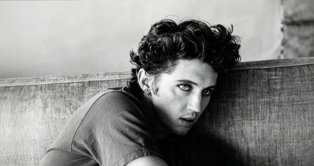 Primo piano in bianco e nero di Troye Sivan con capelli ricci e trucco scuro sugli occhi mentre guarda verso la fotocamera