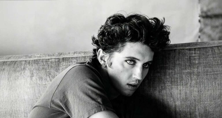 Primo piano in bianco e nero di Troye Sivan con capelli ricci e trucco scuro sugli occhi mentre guarda verso la fotocamera