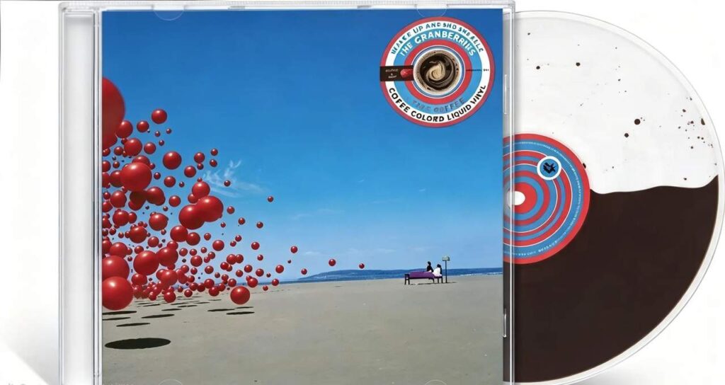 Copertina dell’album Wake Up and Smell the Coffee dei The Cranberries: spiaggia con cielo blu, schiera di palloni rossi a