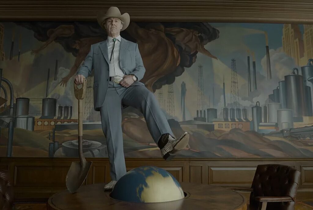 Tom Cruise interpreta il magnate in Digger, in piedi su un globo con una pala davanti a un murale industriale in stile rétro