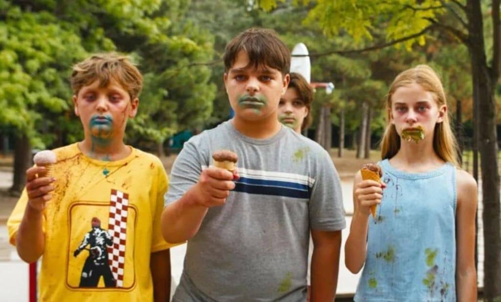 Quattro bambini in un parco con gelati sporchi di colore verde e blu, magliette macchiate e sguardi impassibili