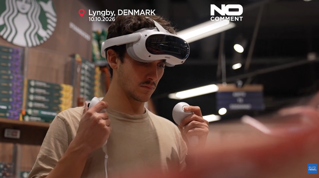 Un uomo indossa un visore VR e impugna due controller in un supermercato, con il logo Starbucks visibile sullo sfondo