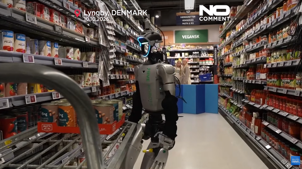 Un robot umanoide Hive Robots spinge un carrello tra gli scaffali di un supermercato in Danimarca, osservato da due persone
