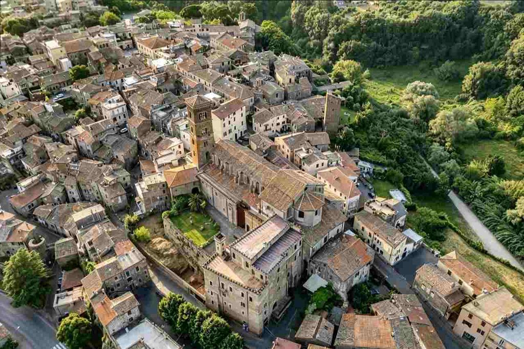 Veduta aerea di un borgo storico del Lazio con chiesa e palazzo medievale in pietra, tetti in cotto e verdeggiante vallata