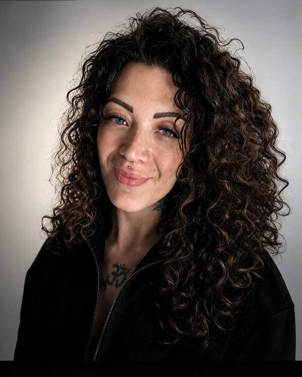 Primo piano di Cristina Giuriolo con lunghi capelli ricci scuri, sguardo diretto e un tatuaggio visibile sul petto