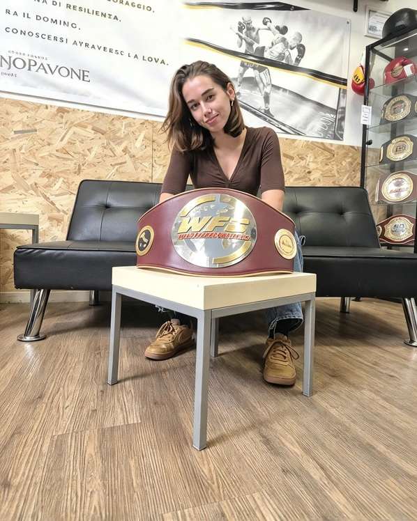 Matilde Crescentini seduta su una panca nera in palestra mentre sorride dietro la cintura da campionessa WFC posata su un