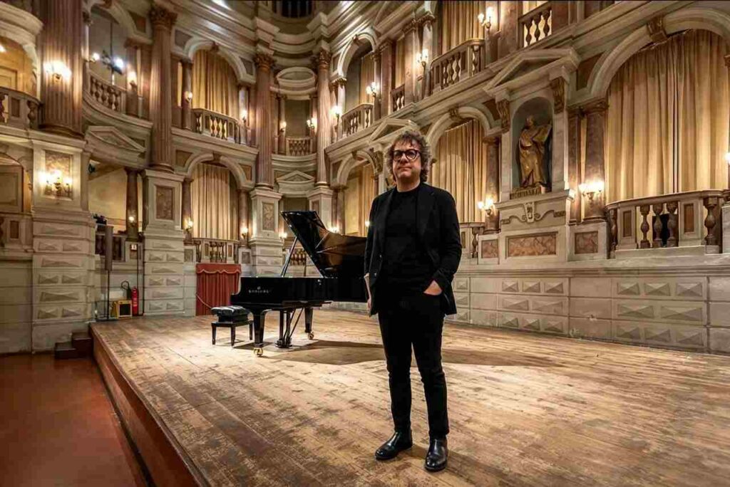 Il compositore Remo Anzovino in piedi sul palco di un teatro storico accanto a un pianoforte a coda nero