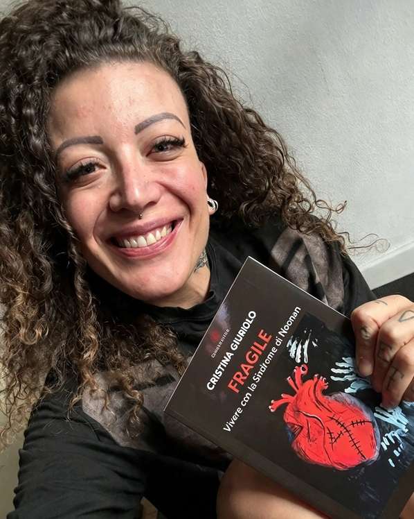 Cristina Giuriolo sorride tenendo in mano il suo libro Fragile: Vivere con la Sindrome di Noonan con l'illustrazione di un