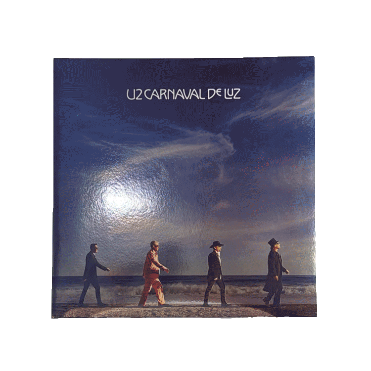Copertina blu con cielo e mare, quattro figure in fila che camminano sulla spiaggia e scritta bianca in alto "U2 Carnaval de