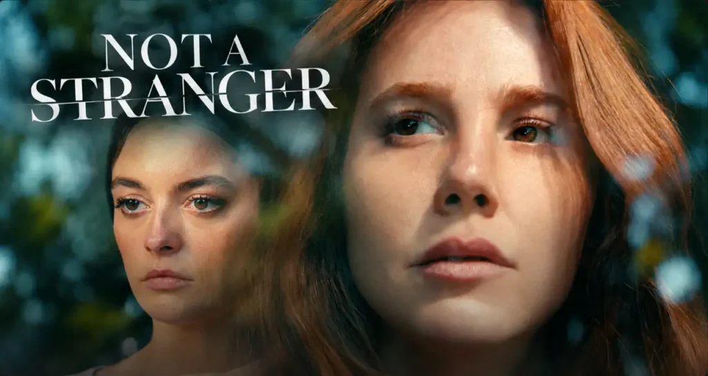 Primo piano di due donne sovrapposte, una rossa in primo piano e una mora sullo sfondo, titolo in inglese "NOT A STRANGER"